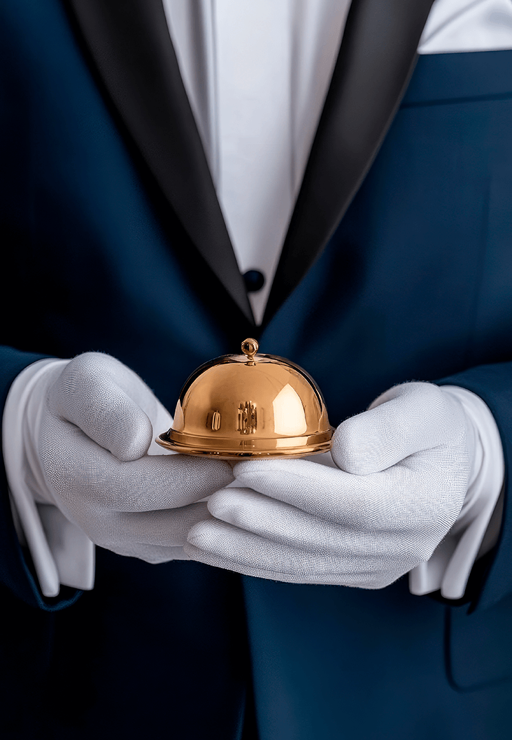 hotel-staff-member-tuxedo-gloves-prepares-ring-service-bell-reception-desk-elegant-lobby-surrounded-by-soft-natural-light